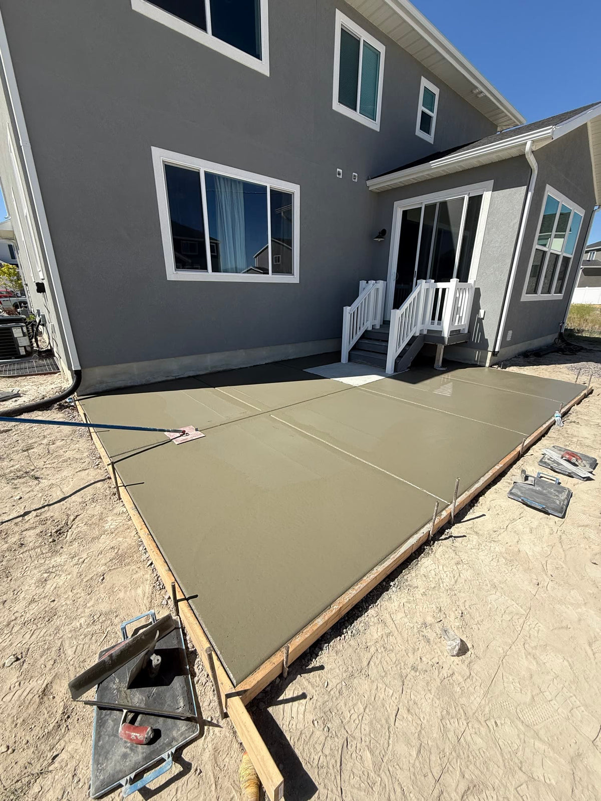 Freshly poured concrete patio slab being finished behind a home in Pleasant Grove, Utah